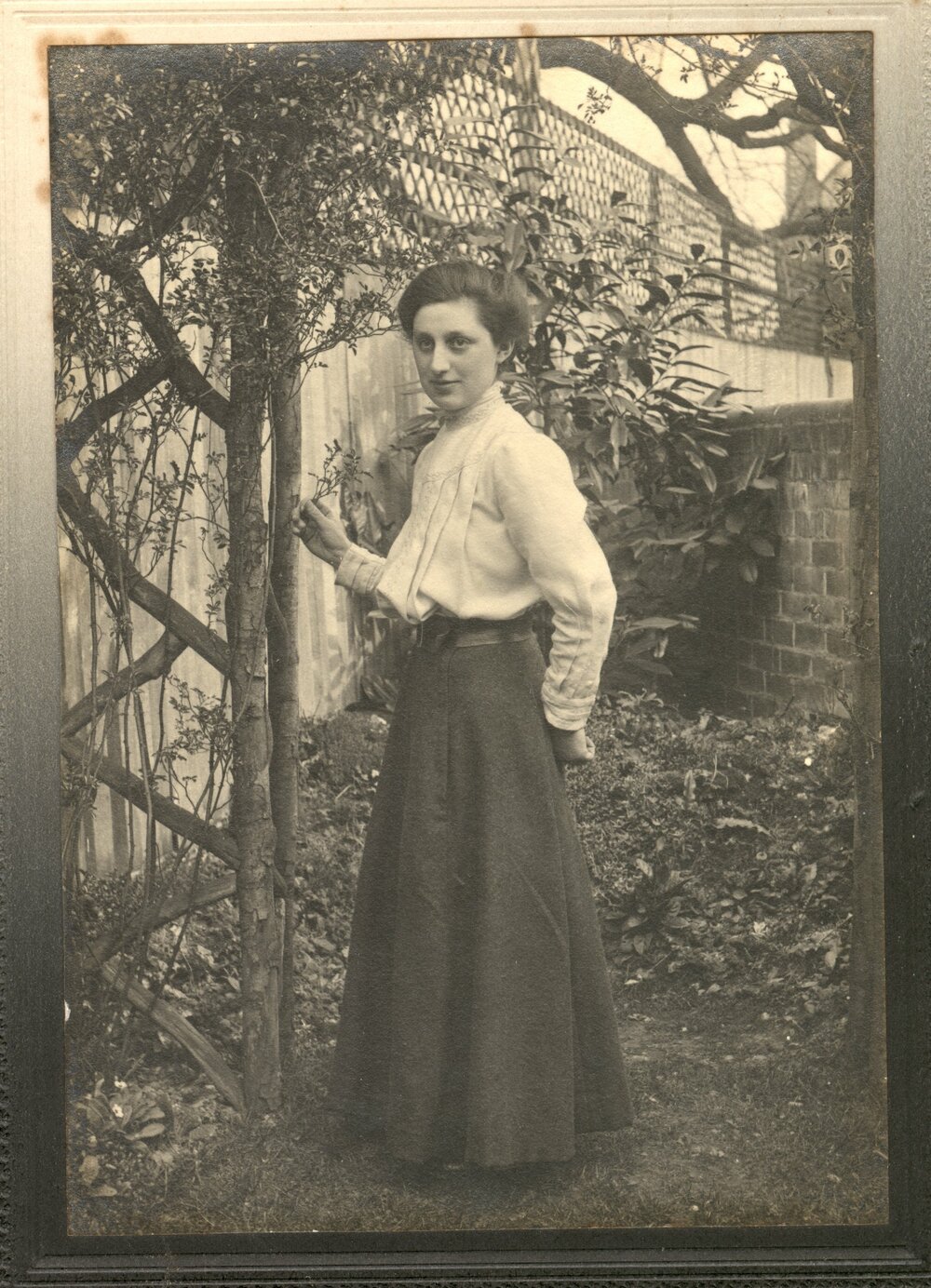 Portrait of Dora in a garden posing by a trellis.  