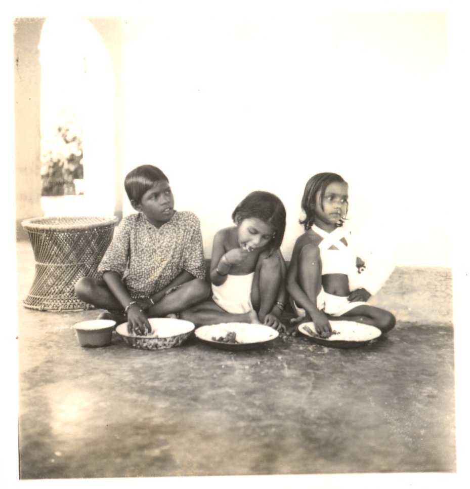 Three Indian children sitting eating rice. 