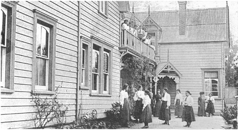 Hukarere School buildings with students in dark skirts and white shirts, with a tennis raquet