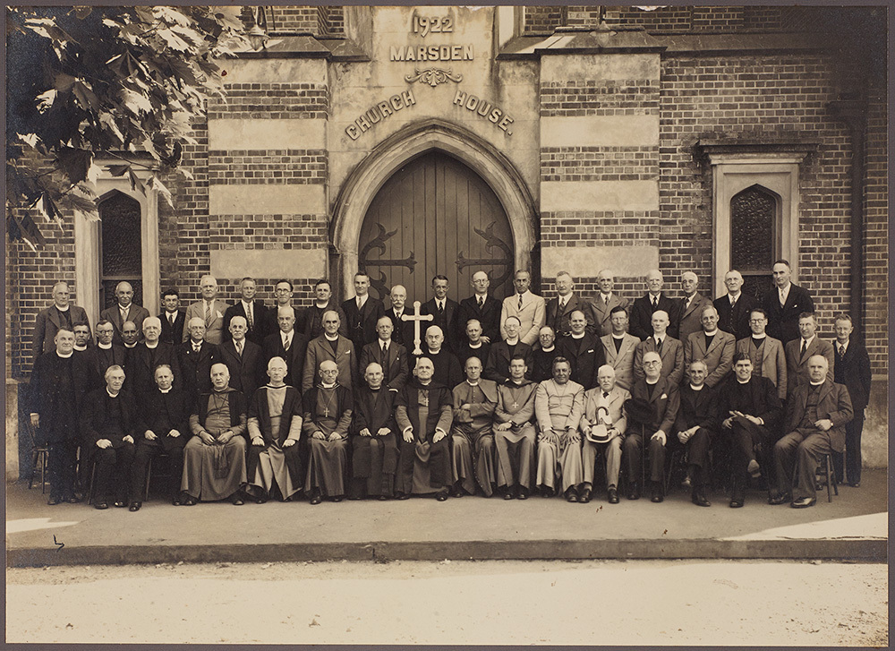 Group of men standing in front of a building which says  Marsden Church House'. 