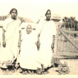 Three Indian women. 1 sitting, 2 standing. 