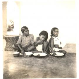 Three Indian children sitting eating rice. 